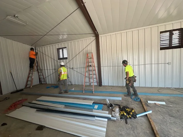 UTS BuildPros crew installing interior liner panel inside a Permian operations and maintenance building, in hard hats and high-visibility vests