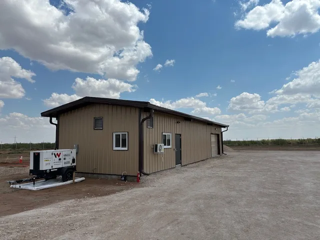 Completed tan metal building with standing-seam roof and a towable generator set alongside, built by UTS BuildPros